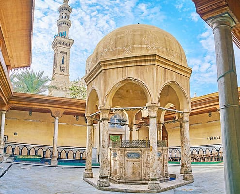 The yard of Imam Busiri Mosque with old stone ablution fountain and minaret of Abu al-Abbas al-Mursi Mosque on background