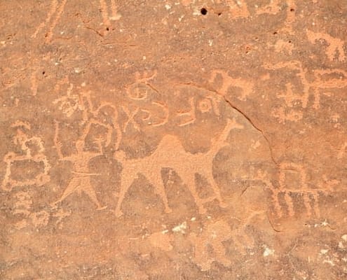 Images of people and camels carved into a rock wall at Wadi Rum