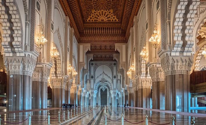 Places to Visit in Casablanca - Hassan II Mosque interior corridor with columns in Casablanca Morocco. Arabic arches, ornaments, chandelier and lighting