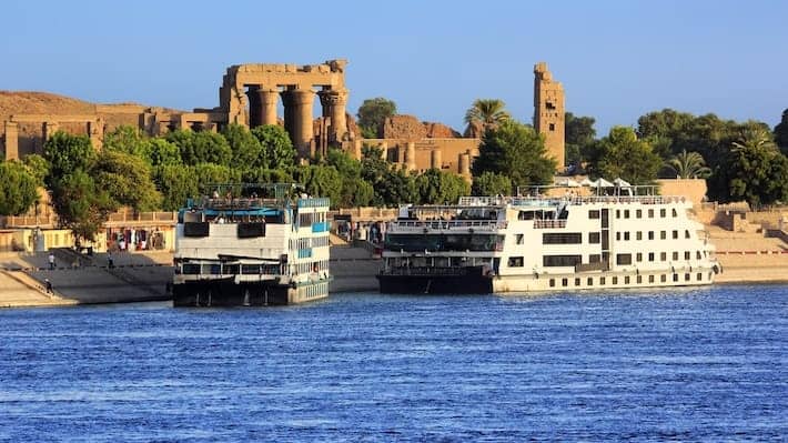 Egypt. Cruise ships docked at Kom Ombo on the Nile. The Temple of Sobek and Haroeris in background - seen colonnade of the Hypostyle Hall