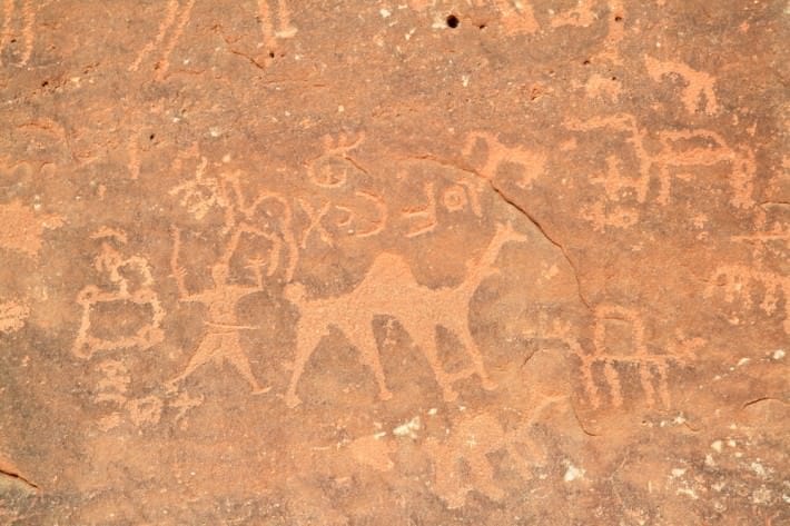 Images of people and camels carved into a rock wall at Wadi Rum